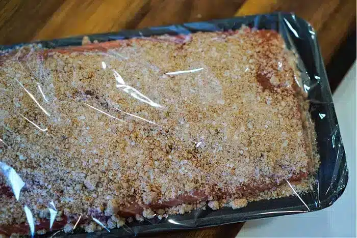 The tray of raw meat, enveloped in a brown breadcrumb seasoning and wrapped in clear plastic, brings to mind the best baked salmon dishes. It rests serenely on a wooden surface, inviting culinary inspiration.