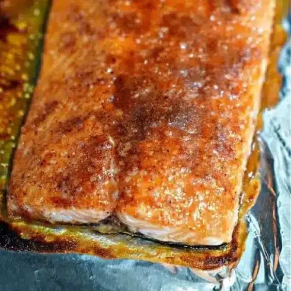 Close-up of the best baked salmon fillet on a foil-covered surface. The fillet has a browned, seasoned crust and glistens, indicating it has been recently cooked. The foil showcases some caramelized sauce around the edges, enhancing its perfect presentation.