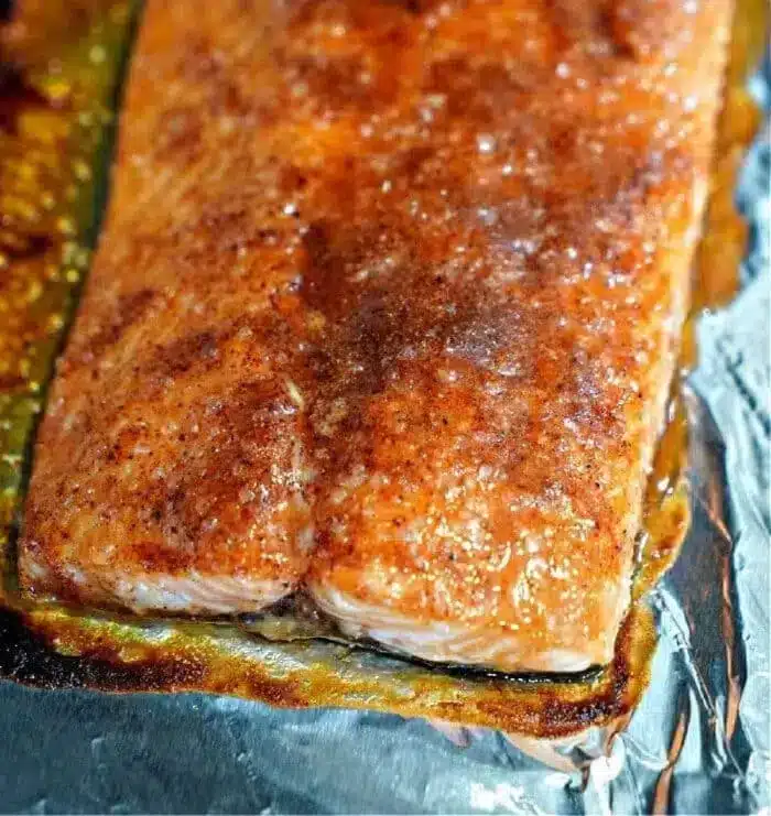 Close-up of the best baked salmon fillet on a foil-covered surface. The fillet has a browned, seasoned crust and glistens, indicating it has been recently cooked. The foil showcases some caramelized sauce around the edges, enhancing its perfect presentation.