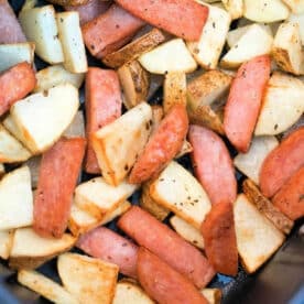 Cubed potatoes and sliced sausage, seasoned and cooked together in the air fryer with crispy pieces of Spam, shown in a close-up shot.