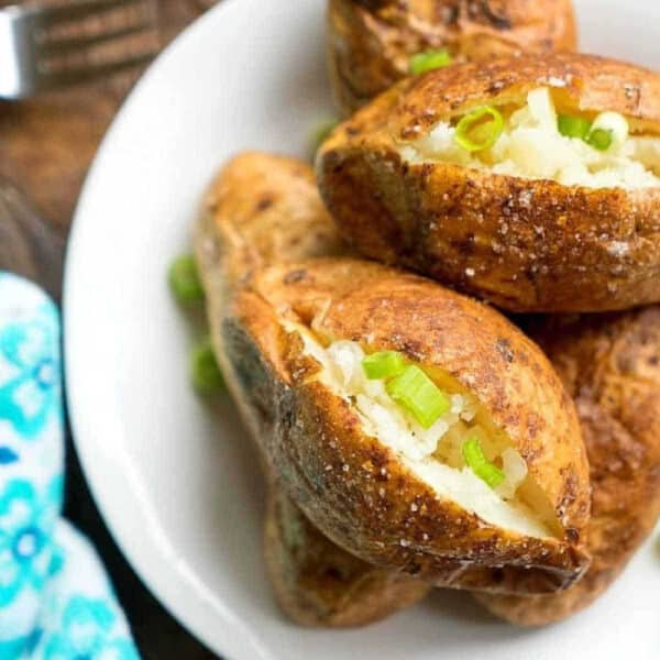 Baked potatoes without foil topped with chopped green onions on a white plate.
