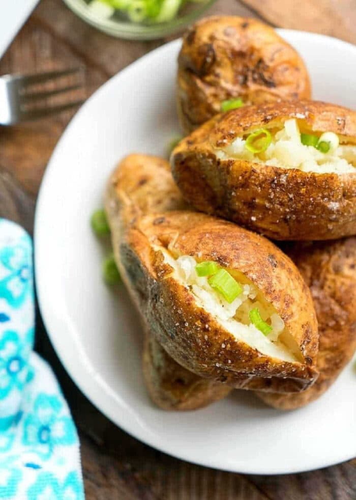 This is the best way to make baked potatoes so they're tender and fluffy on the inside with crispy flavorful potato skins! Used as a side dish or dinner stuffed with chili or cheese they're delicious and cheap to make. If you're looking for an easy baked potato recipe I've got it here. #bakedpotatoes #howtomake #perfect #potatoes #baked #sidedish #healthy #easy Baked potatoes without foil topped with chopped green onions on a white plate.