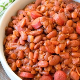 A rustic bowl of Beans and Weenies, showcasing baked beans with sliced hot dogs, sits invitingly on a wooden surface.