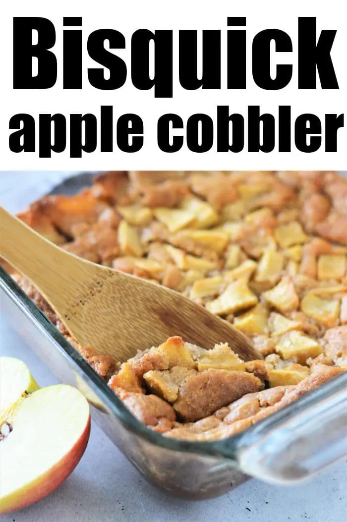 A glass baking dish filled with apple cobbler. A wooden spoon is scooping up a portion. The top text reads "Apple Cobbler with Bisquick." Two apple slices are visible next to the dish on the left side of the image.