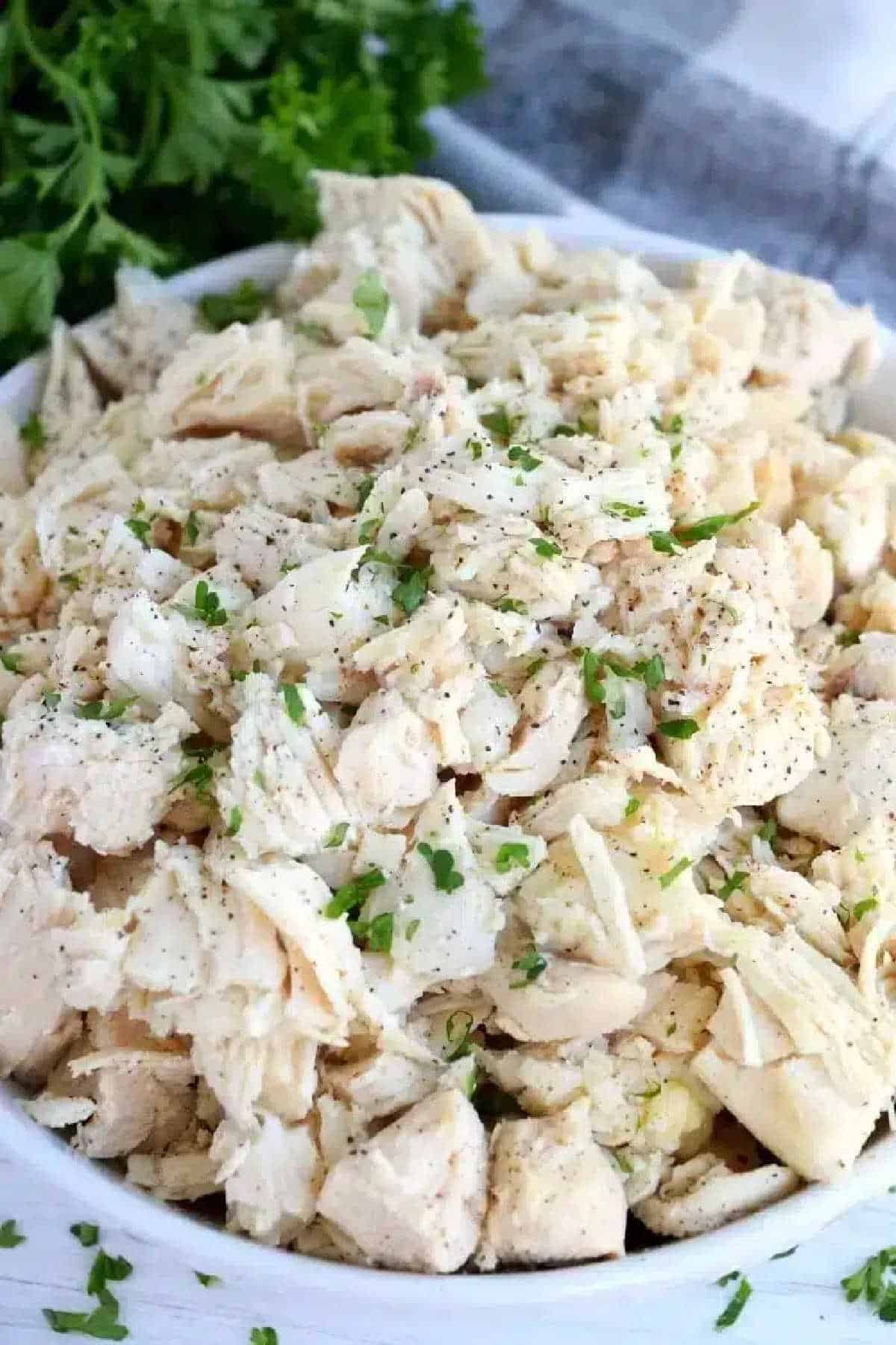 A bowl of shredded cooked chicken, garnished with chopped parsley and black pepper—perfect for anyone learning how to make shredded chicken on the stove.
