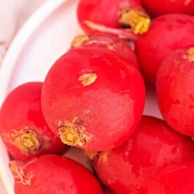 Close-up of red radishes on a white plate, ready for culinary exploration. Imagine how vibrant they'd look after learning how to cook radishes in a Ninja Foodi, transforming them into a delightful dish with ease.