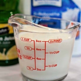 A measuring cup filled with milk, the first step in how to make buttermilk with lemon juice, stands surrounded by zesty lemon juice and milk carton containers.