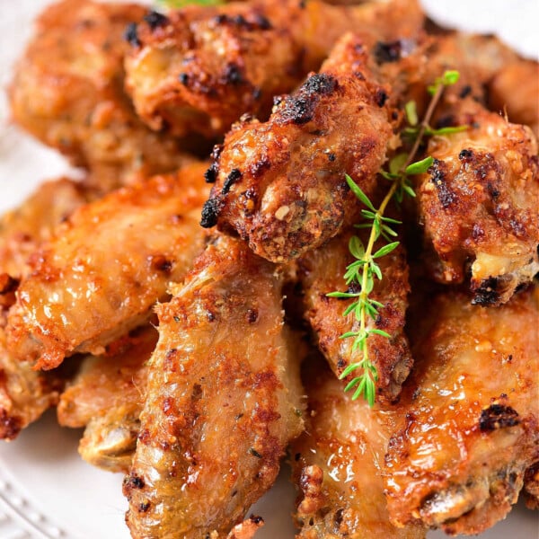 A plate filled with crispy, golden-brown chicken wings garnished with a sprig of thyme. The wings appear to be well-seasoned and cooked with a slightly charred exterior, indicating they were either baked or fried. Perfect for those wondering *how to reheat food in an air fryer* for that irresistible crunch.