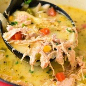 A ladle scooping creamy chicken poblano soup with vegetables from a pot.