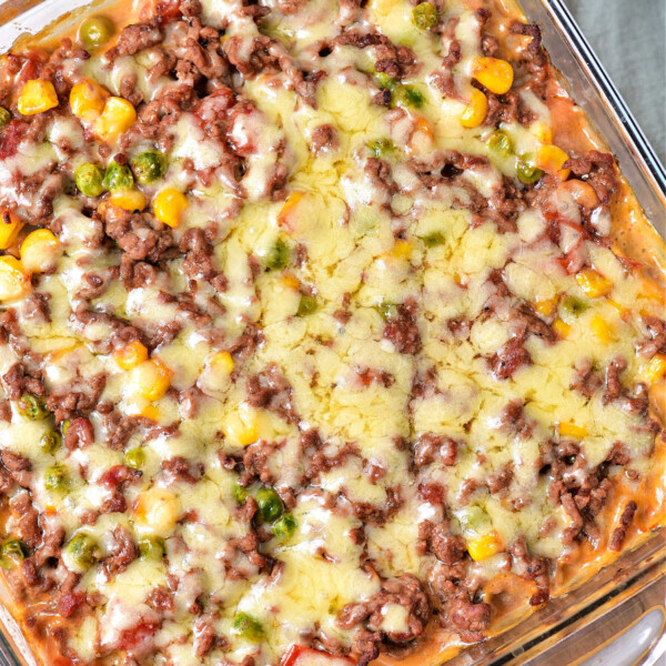 The ShipWreck Casserole is a delightful baked dish featuring ground meat, melted cheese, corn, peas, and tomatoes all layered beautifully in a square glass dish.