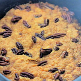 A close-up of pumpkin cake topped with pecans in a black crockpot, reminiscent of a comforting pumpkin dump cake.