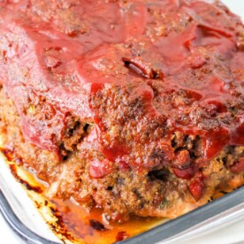 A freshly baked spicy meatloaf in a glass dish, topped with zesty tomato sauce.