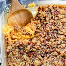 A glass dish with a delectable sweet potato casserole recipe featuring canned yams, topped with crunchy pecans and accompanied by a wooden spoon.