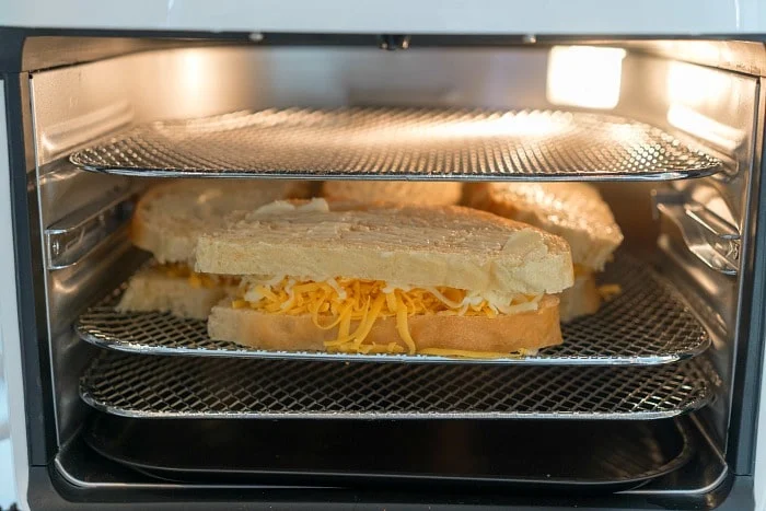 Several uncooked grilled cheese in air fryer sandwiches rest on wire racks inside the oven, ready to be toasted to golden perfection.