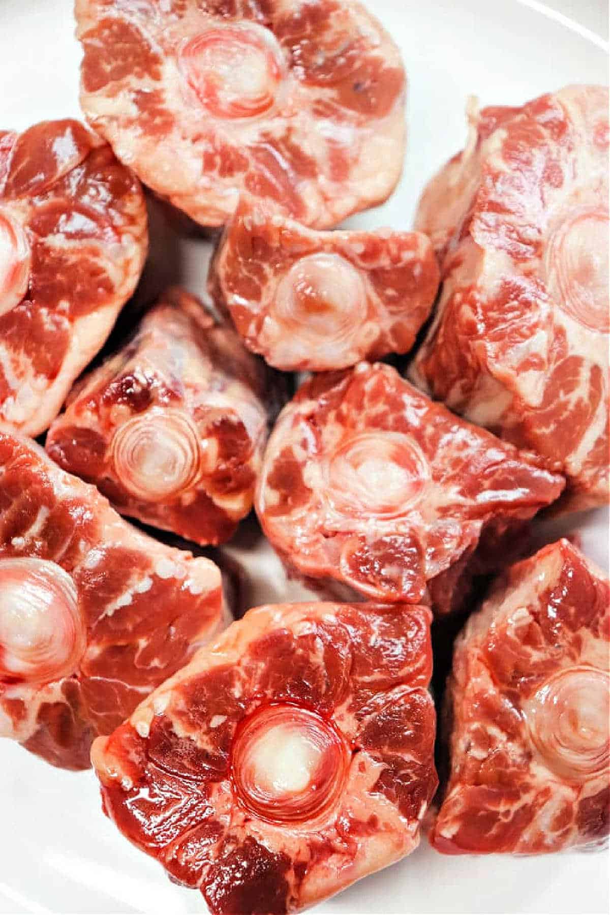 Raw oxtail pieces arranged on a white plate, showcasing marbled meat and circular bone centers, inviting you to explore how to cook oxtails for a rich and savory dish.