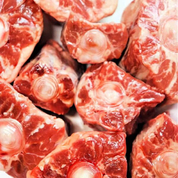 Raw oxtail pieces rest on a white plate, showcasing their marbled fat and bone—a perfect starting point for anyone curious about how to cook oxtails.