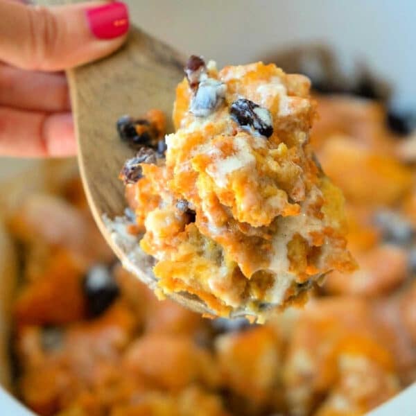 A wooden spoon holds a serving of crockpot bread pudding with raisins above a slow cooker.