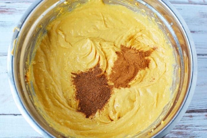 Pumpkin batter in a metal bowl with cinnamon and nutmeg sprinkled on top, ready to be baked into a delicious sheet pan pumpkin pie.