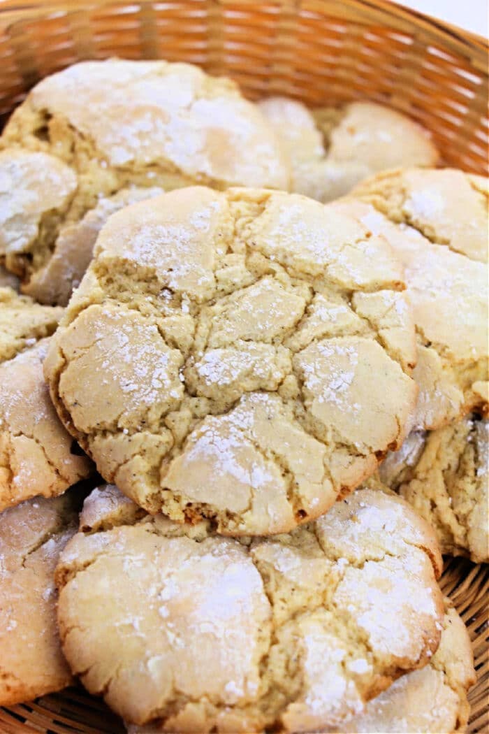 A close-up photo of a basket filled with large, cracked, and powdered sugar-coated Vanilla Cake Mix Cookies. The cookies are golden-brown with a rough, crumbly texture and appear freshly baked.