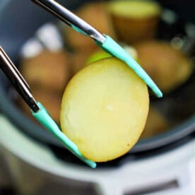 Close-up of tongs lifting a perfectly cooked potato slice from the bubbling Instant Pot.