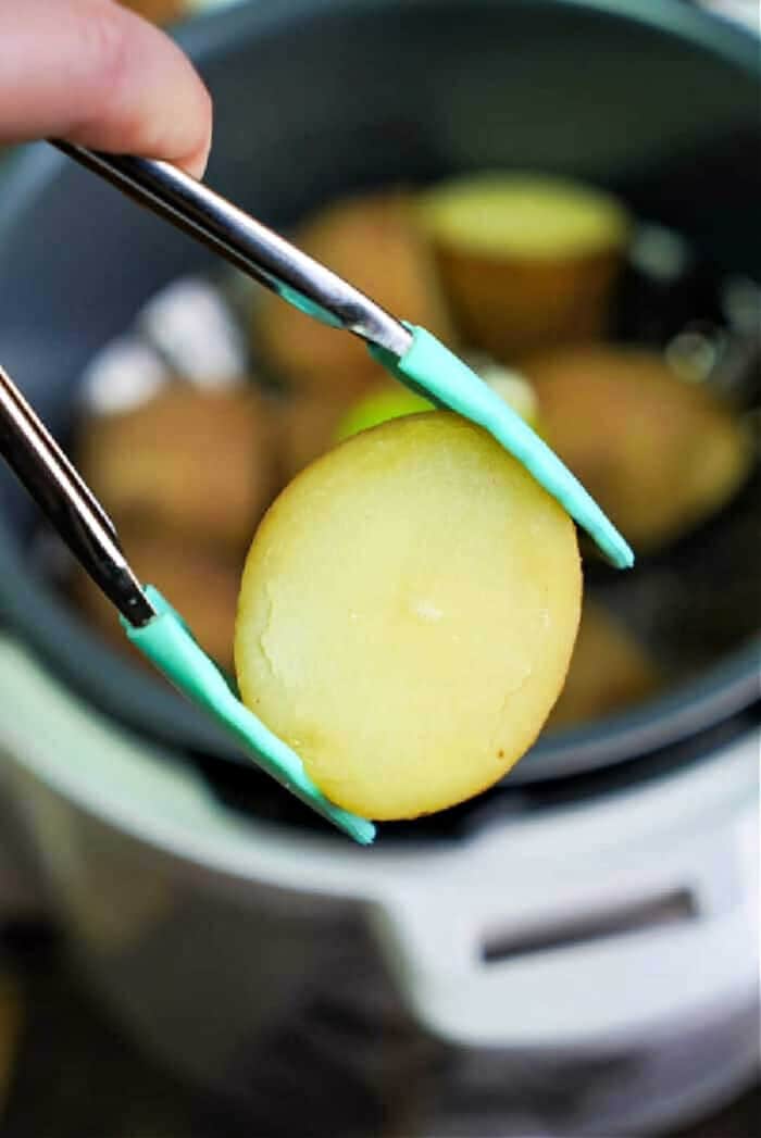 Close-up of tongs lifting a perfectly cooked potato slice from the bubbling Instant Pot.