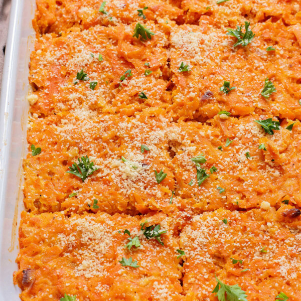 Baked carrot casserole topped with breadcrumbs and parsley in a white dish, cut into portions.