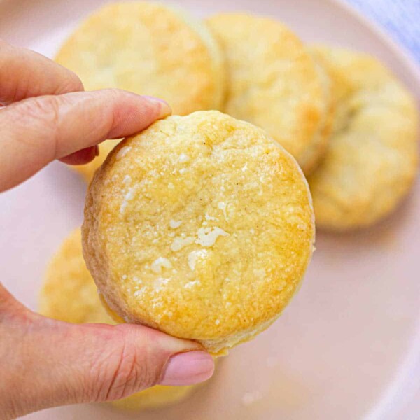 A hand holding a freshly baked Dutch Oven biscuit over a plate of warm, golden biscuits.