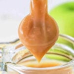 A close-up image shows a spoon dripping luscious caramel sauce into a glass jar. The background features a green blurred object. The text at the top reads, "How to Make Dulce de Leche in a Pressure Cooker.