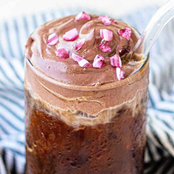 Iced coffee topped with a layer of thick, peppermint chocolate cream cold foam and pink sprinkles, served with a clear straw.