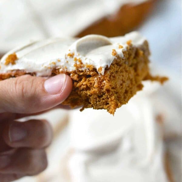 Close-up of a hand holding pumpkin bars made with cake mix, and more cake pieces in the background.