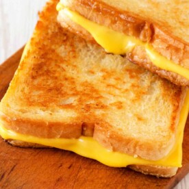 Two golden brown grilled cheese sandwiches, perfectly crisp from the toaster oven, are stacked on a wooden board.