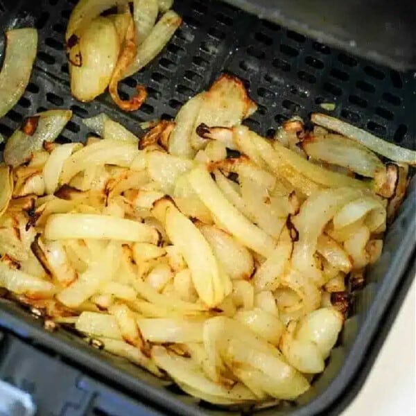 Sliced onions are being expertly cooked and slightly browned in the air fryer basket, transforming into deliciously crispy air fryer onions.