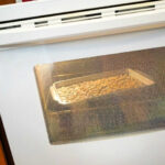 Image of a white oven with a tray of pumpkin seeds roasting inside.