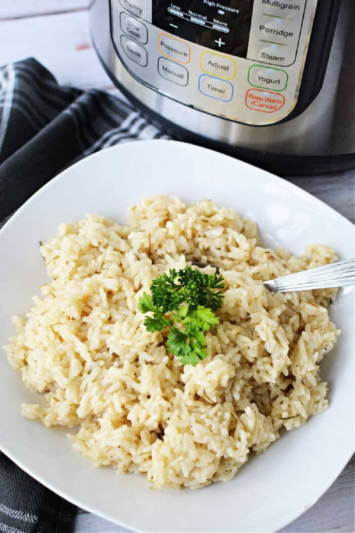 A plate of cooked risotto garnished with parsley sits next to an Instant Pot, showcasing a delicious instant pot risotto recipe, with a fork placed on the plate for easy serving.