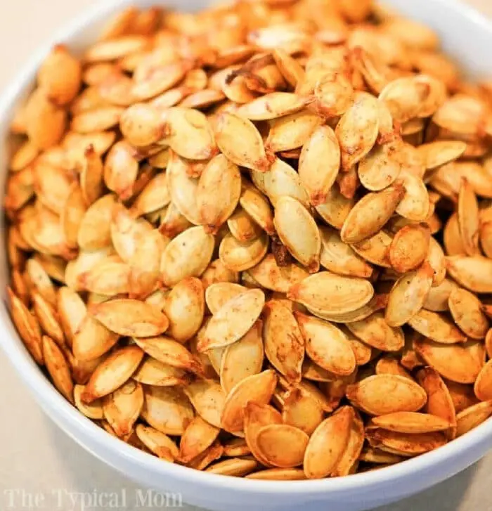 A white bowl filled with a large quantity of seasoned, roasted air fryer pumpkin seeds. The seeds appear golden brown and are seasoned with various spices. 