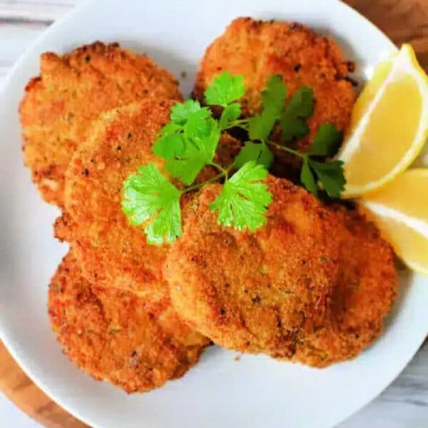 Five golden brown Air Fryer Crab Cakes garnished with cilantro and lemon wedges on a white plate.