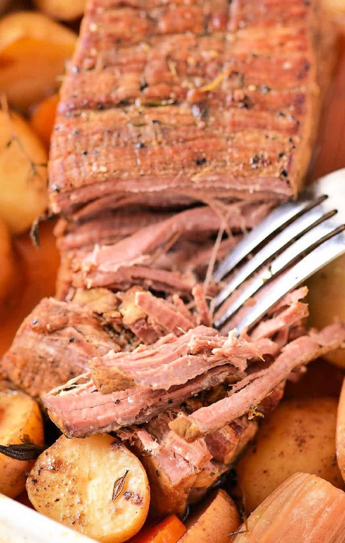 A fork shredding tender, cooked pot roast with potatoes and carrots in the background—discover how long to cook chuck roast in oven at 350 for perfectly juicy results every time.