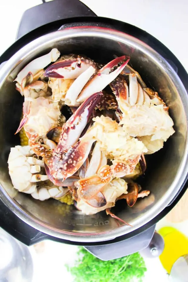 A bowl filled with partially cooked crab pieces shows visible crab shells and sections of white crab meat. The metal edges suggest it might be part of a cooking appliance or pot.