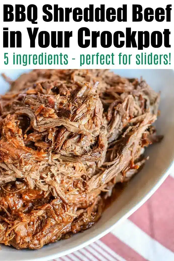 A close-up of a dish featuring crockpot BBQ shredded beef. The text at the top reads: "BBQ Shredded Beef in Your Crockpot" followed by "5 ingredients - perfect for sliders!" The beef is served on a white plate with a red and white striped cloth underneath.