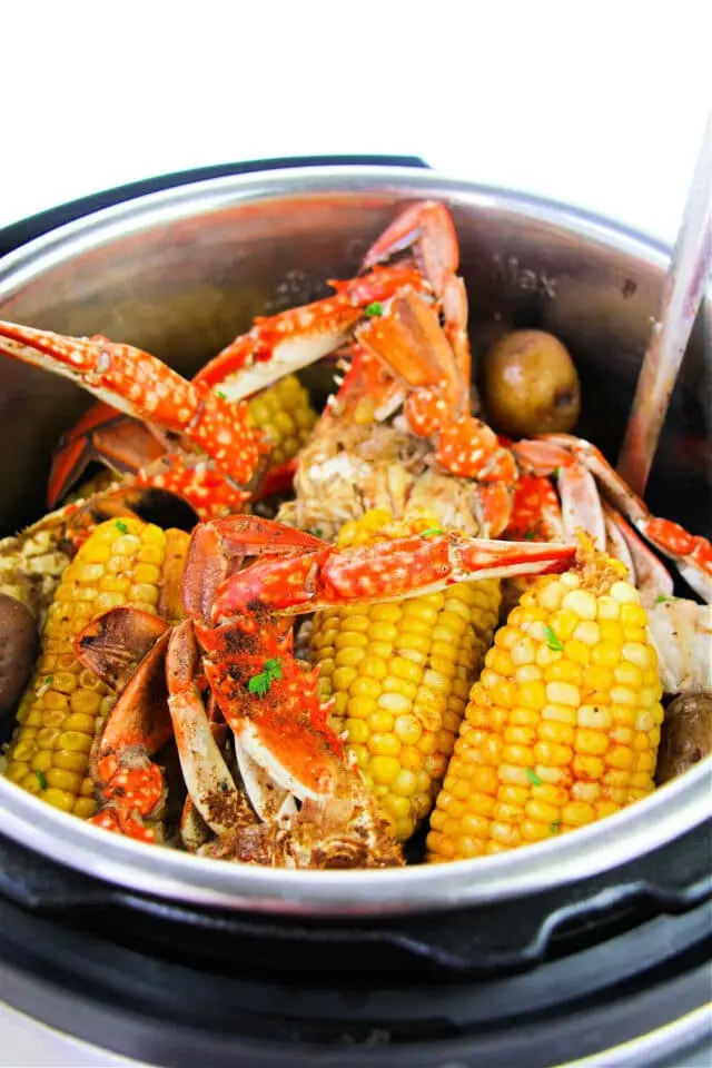 A metal pot filled with cooked crabs, corn on the cob, and potatoes.