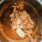 Shredded cooked chicken in sauce sits inside an open pressure cooker or Instant Pot on a kitchen counter, similar to how you might prepare instant pot turkey tenderloin for a quick and flavorful meal.