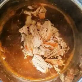 Shredded cooked chicken in sauce sits inside an open pressure cooker or Instant Pot on a kitchen counter, similar to how you might prepare instant pot turkey tenderloin for a quick and flavorful meal.