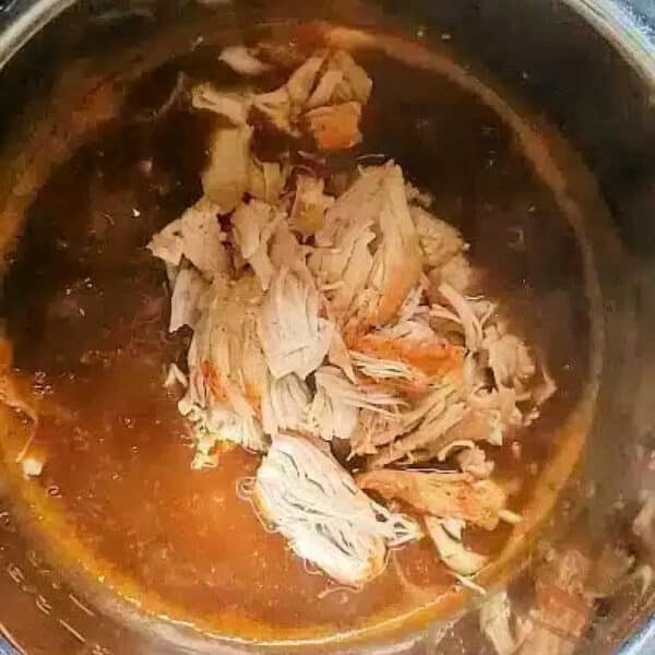 Shredded cooked chicken in sauce sits inside an open pressure cooker or Instant Pot on a kitchen counter, similar to how you might prepare instant pot turkey tenderloin for a quick and flavorful meal.