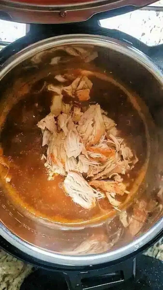 Shredded cooked chicken in sauce sits inside an open pressure cooker or Instant Pot on a kitchen counter, similar to how you might prepare instant pot turkey tenderloin for a quick and flavorful meal.