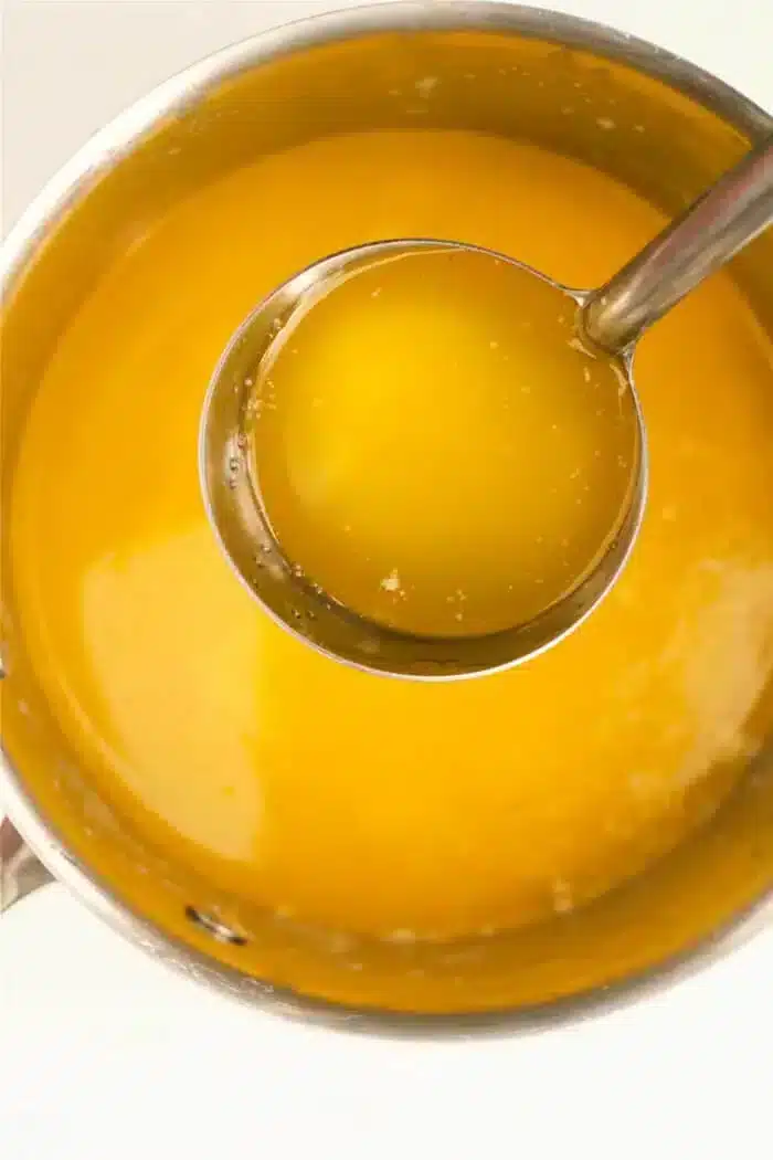 A metal pot brimming with liquid butter, with a silver ladle partially lifted out, reveals the golden yellow richness inside.