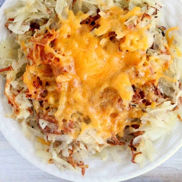 A plate of crispy, oven-baked frozen hash browns topped with melted cheddar cheese.