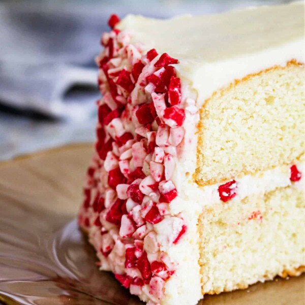 A slice of white cake with peppermint frosting and red and white sprinkles sits elegantly on a plate.