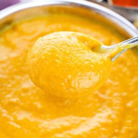 A spoon holding thick, creamy Pumpkin Soup with Canned Pumpkin hovers over a bowl filled with the same golden curry sauce.