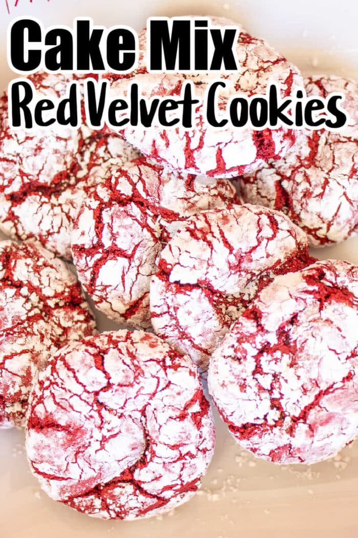A pile of Red Velvet Crinkle Cookies coated in powdered sugar is pictured. The text at the top reads "Cake Mix Red Velvet Cookies." The cookies have a cracked appearance, with red velvet showing through the white powdered sugar.