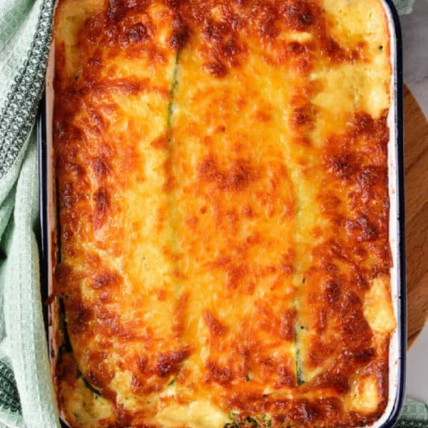 Golden-brown baked vegetable lasagna with white sauce in a rectangular dish, wrapped with a green textured kitchen towel.